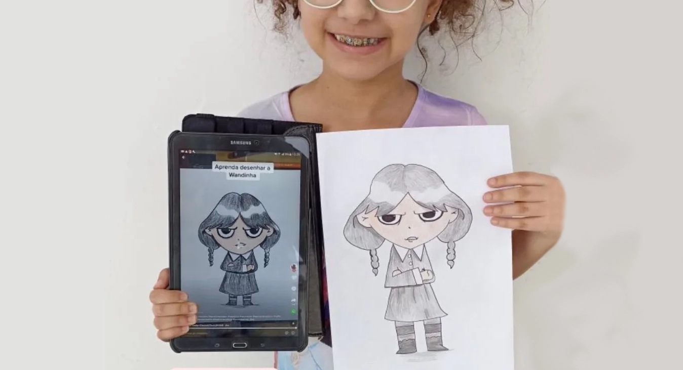 Laura, aluna do curso, segurando o tablet com a aula e o desenho que ela fez